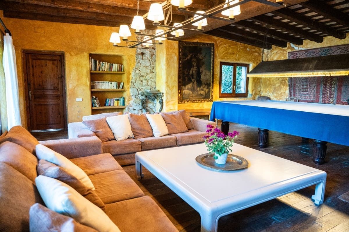 Sala de estar rústica con sofá modular color beige, mesa de centro blanca, mesa de billar con cubierta azul y chimenea de piedra.