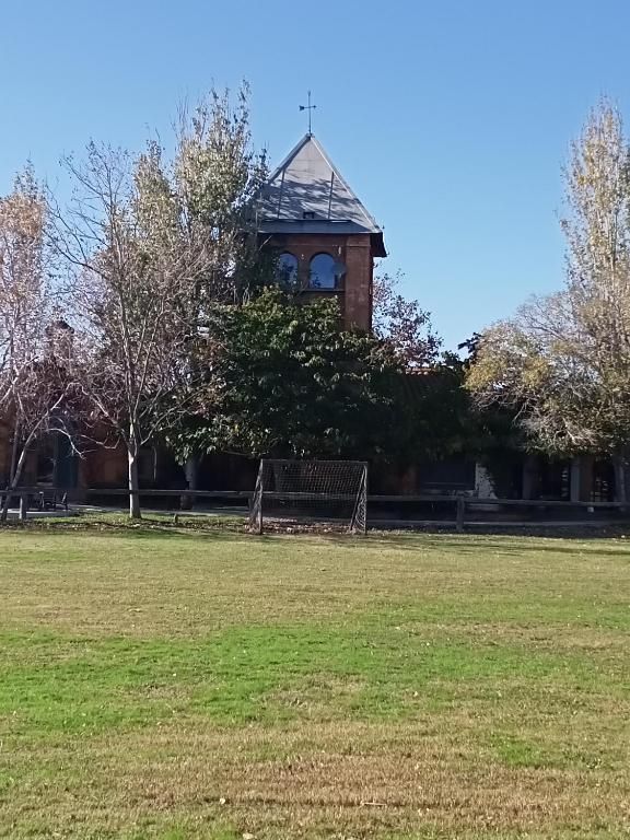 Edificio de ladrillo con una torre central detrás de un campo de hierba y árboles bajo un cielo azul claro.