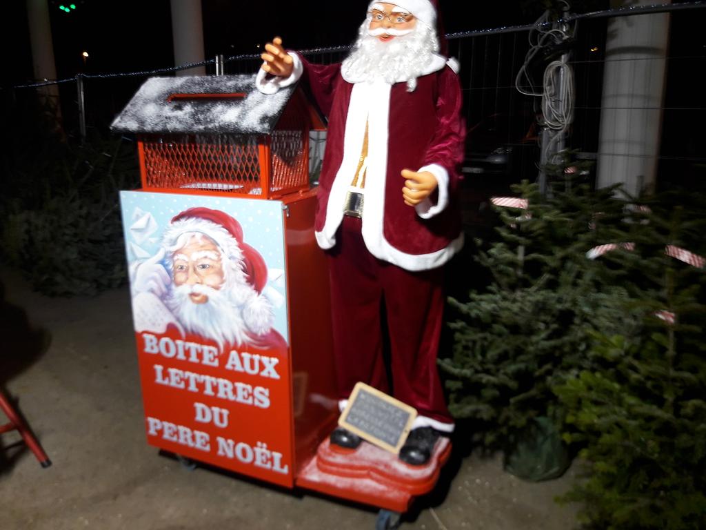 Père Noël à côté de sa boîte aux lettres et entouré de sapins