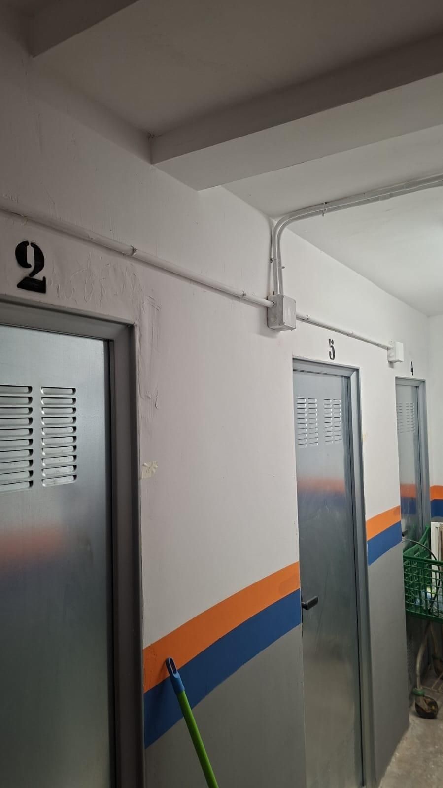 Puertas con los números 2, 3 y un 4 parcial. El conducto eléctrico corre a través de la pared blanca con rayas naranjas y azules.