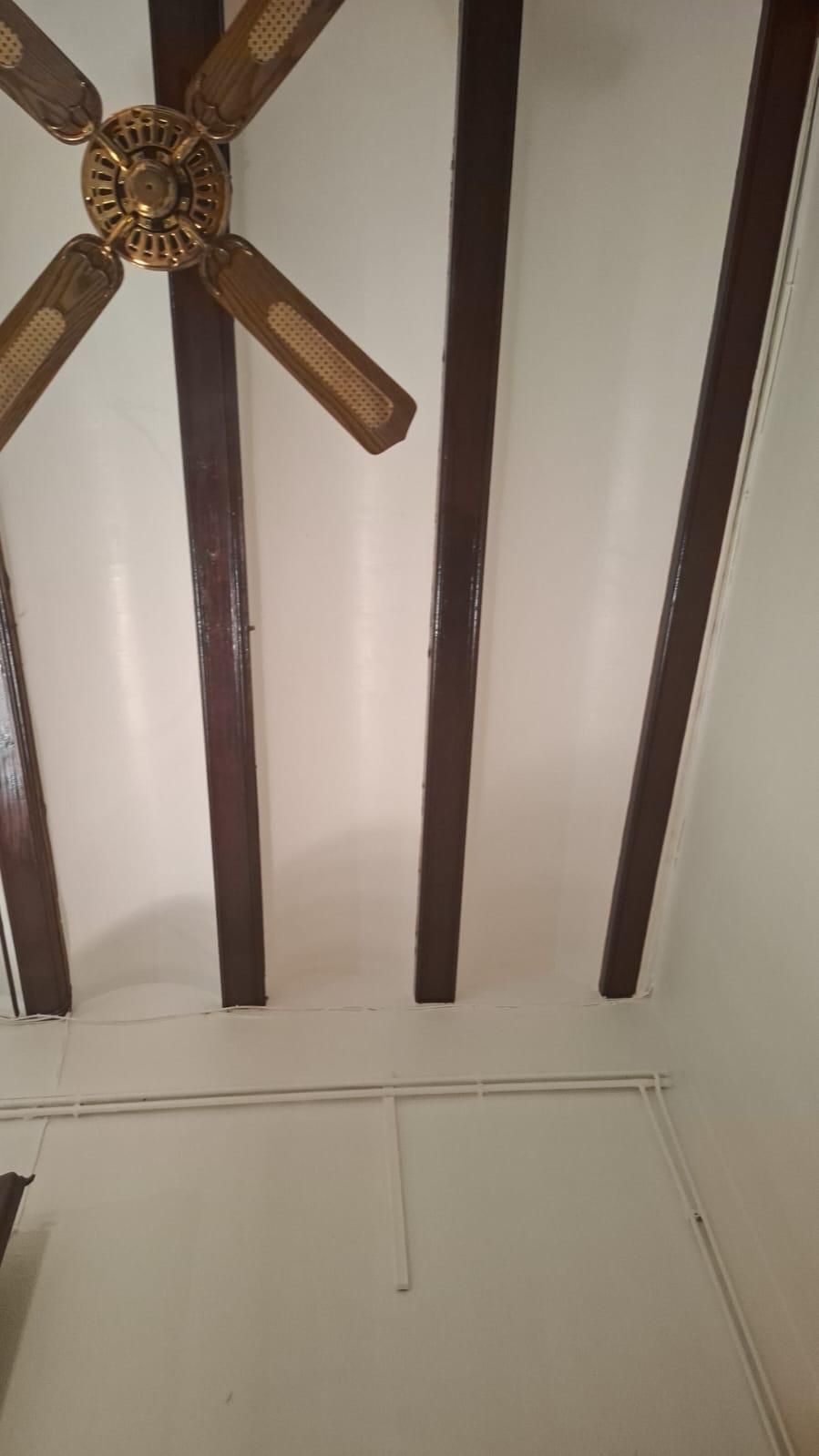 Techo con vigas de color marrón oscuro, paredes blancas y un ventilador de techo dorado.