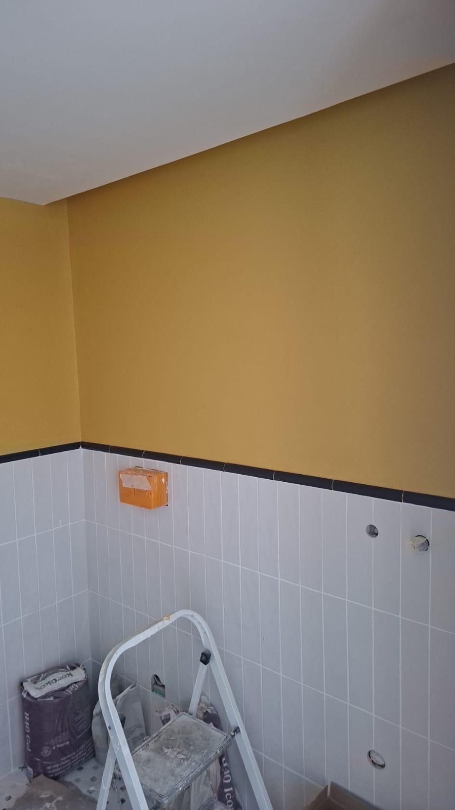 Baño en renovación con paredes amarillas, azulejos blancos, molduras negras y una escalera de mano.