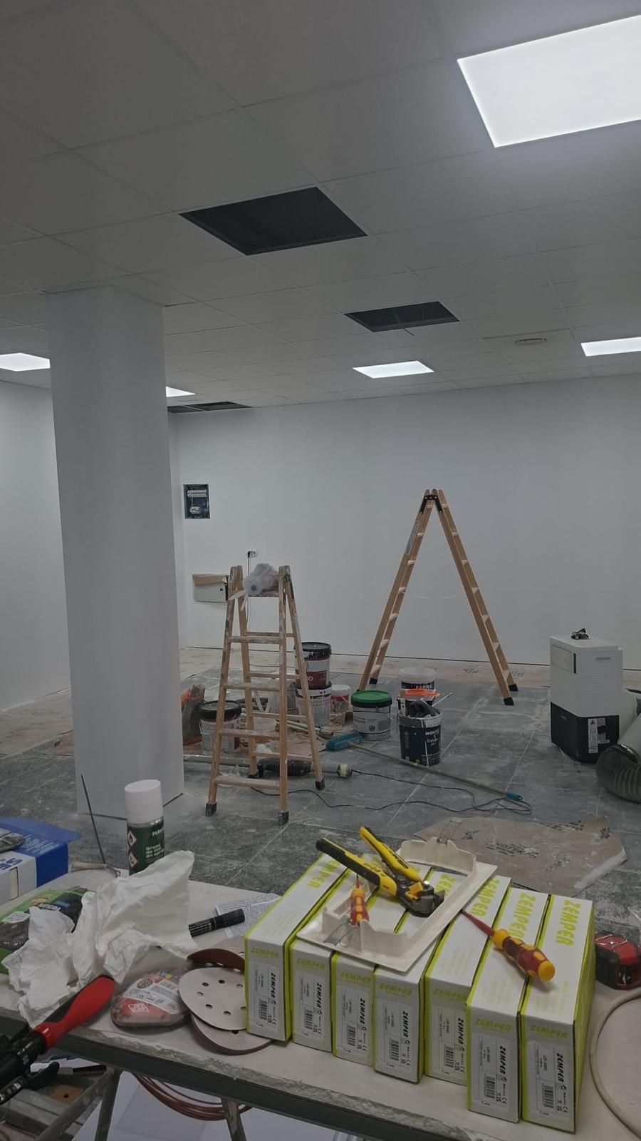 Habitación interior en remodelación, paredes blancas, escaleras, herramientas y útiles esparcidos.