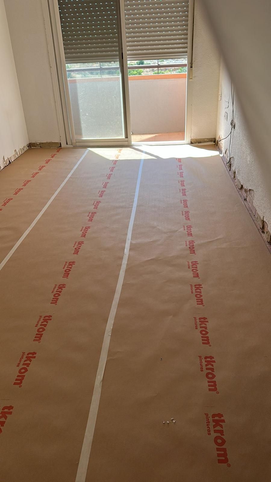 Habitación con papel protector de piso marrón, puerta corrediza de vidrio al balcón.