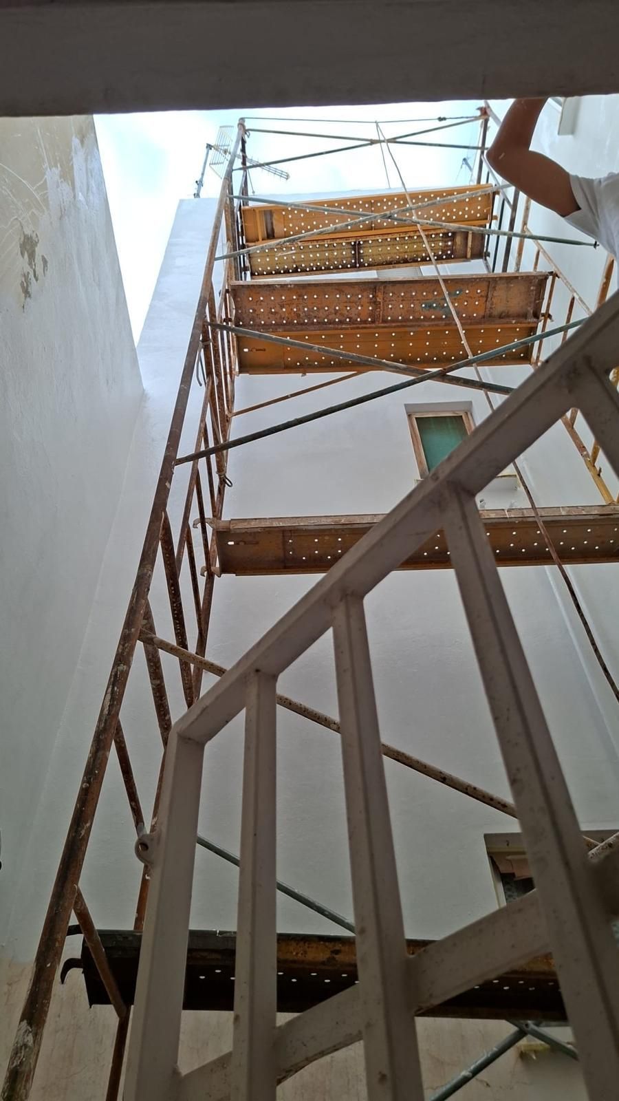 Andamio frente a un edificio blanco; cerca de la parte superior se ve el brazo de una persona.