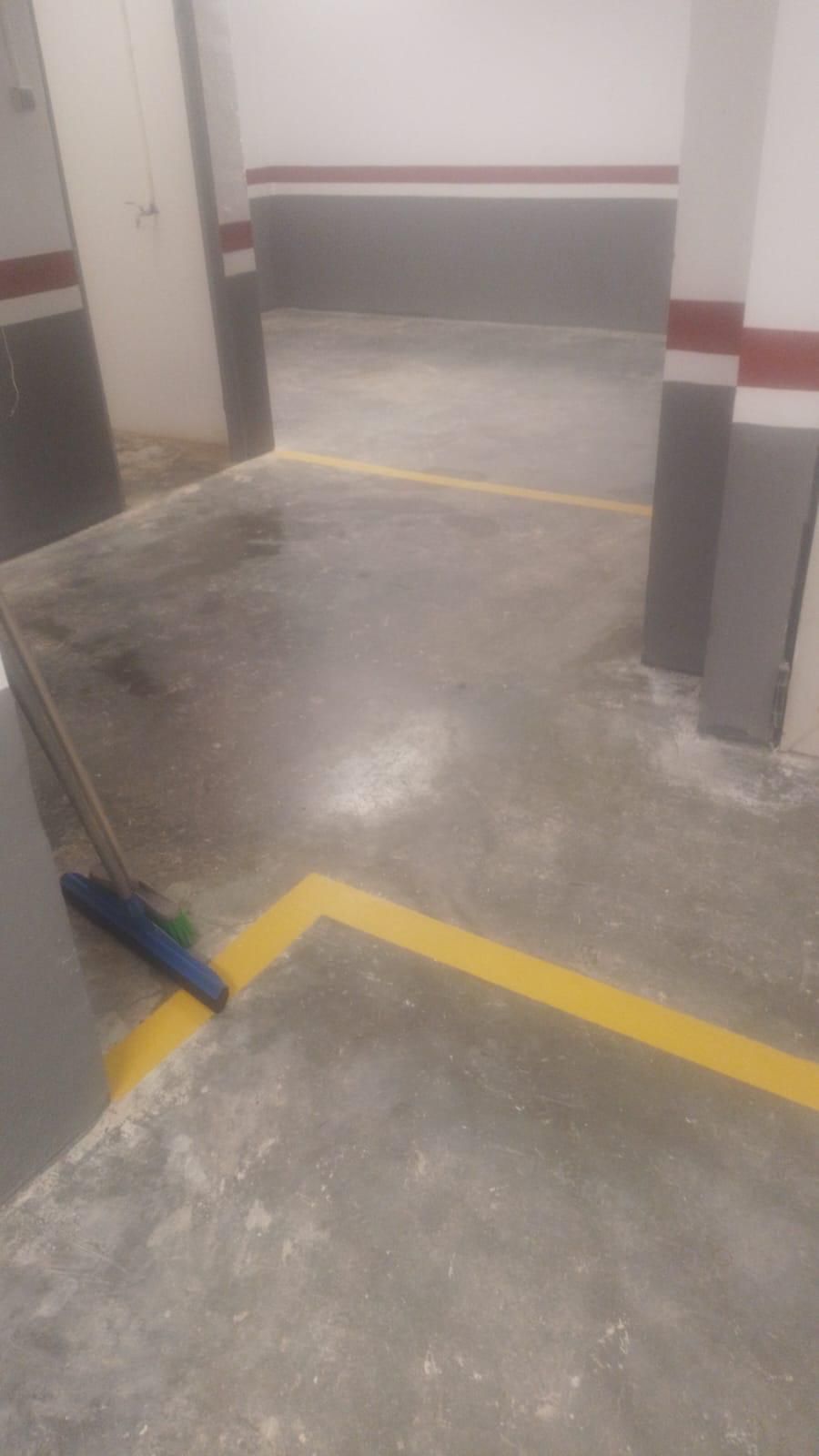 Estacionamiento de concreto con líneas amarillas, paredes grises y detalles en rojo y blanco en las columnas de soporte.