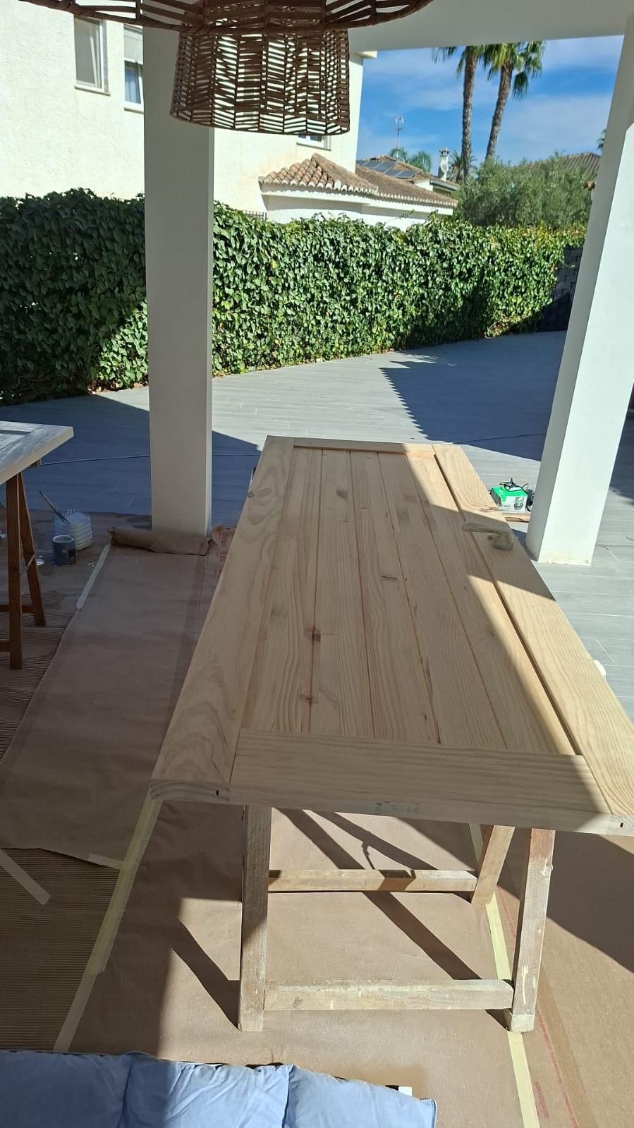 Puerta de madera colocada sobre un caballete en un entorno exterior con vegetación y columnas blancas.