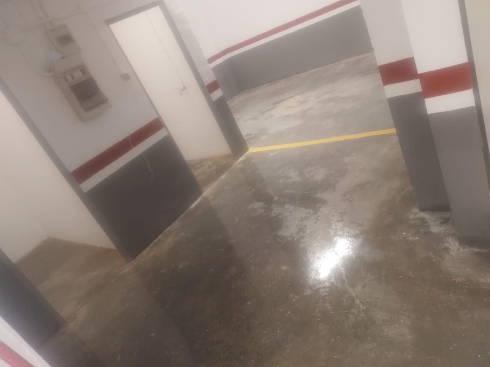 Estacionamiento interior, piso de concreto gris, paredes blancas y grises con franjas rojas, línea amarilla.