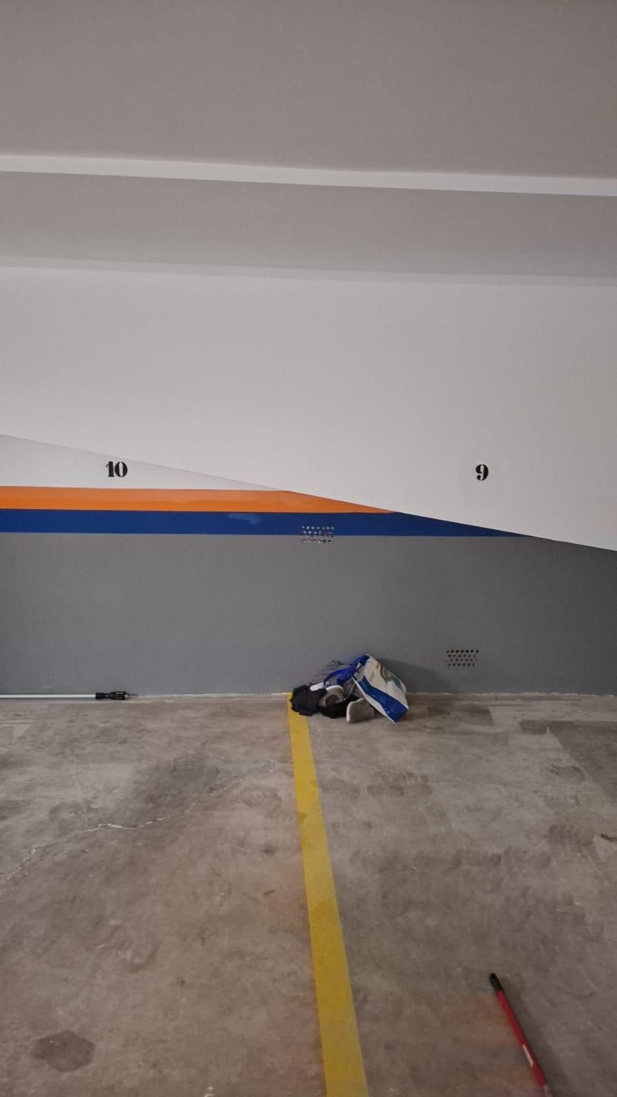 Suelo de hormigón con línea amarilla y pared pintada en naranja, azul y gris. Bolsa y objetos en el suelo.