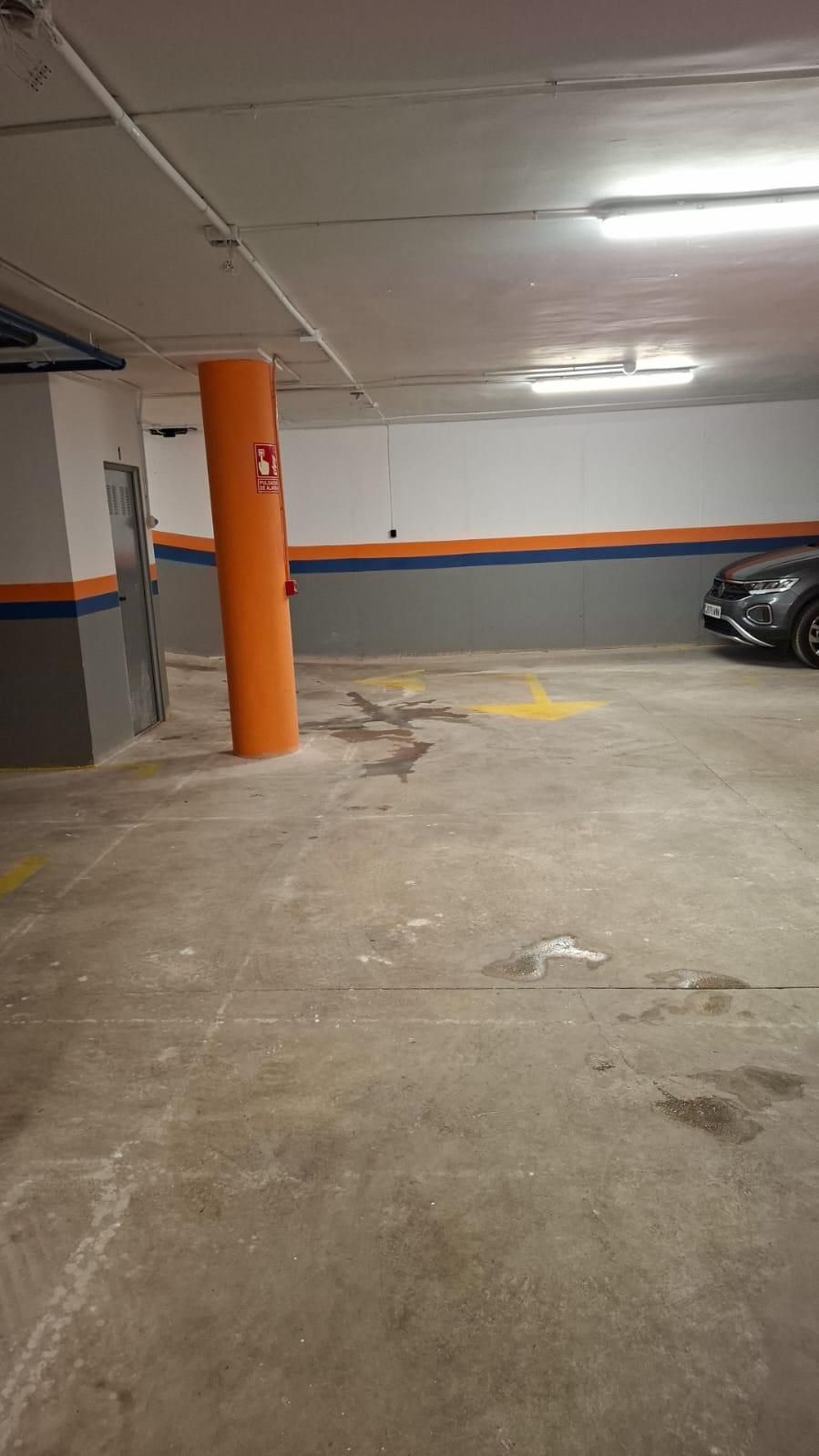 Estacionamiento subterráneo con piso de concreto, pilar naranja, paredes pintadas de gris y naranja y un auto estacionado.