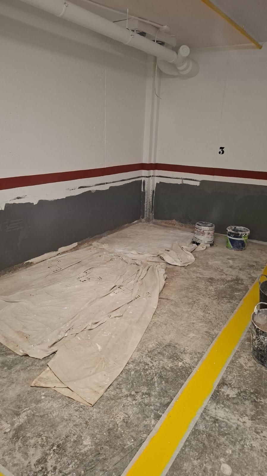 Interior de habitación con suelo de hormigón gris, paredes blancas y grises, molduras rojas. Lienzo blanco sobre el suelo y botes de pintura.