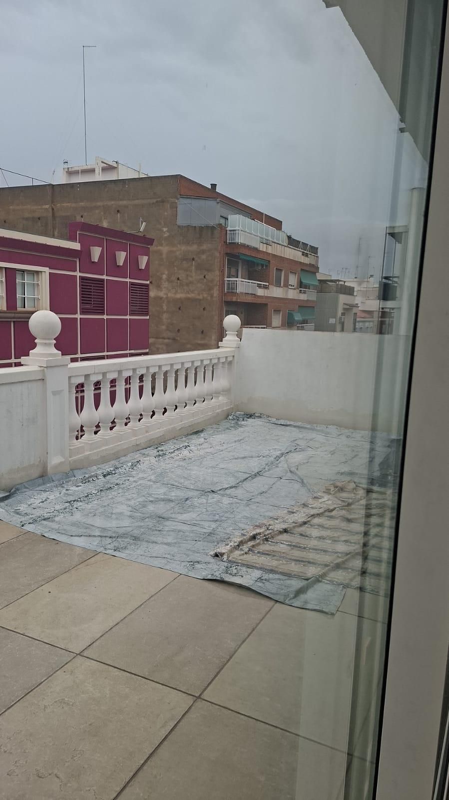 Patio en la azotea con barandilla blanca, cubierto con lona. Edificios al fondo, cielo nublado.