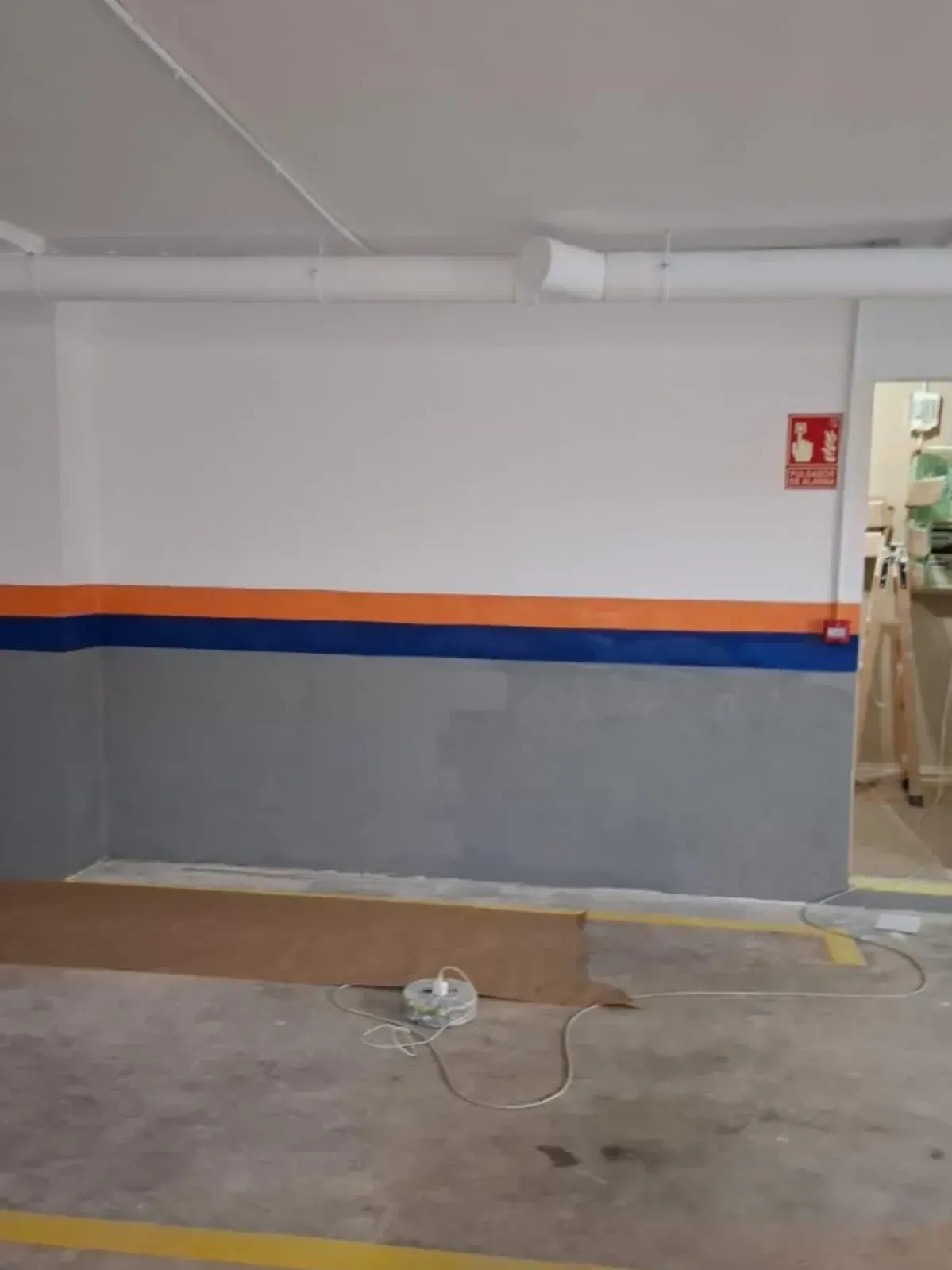 Interior de garaje con paredes pintadas de blanco, gris y naranja, cartel de extintor y cable eléctrico.