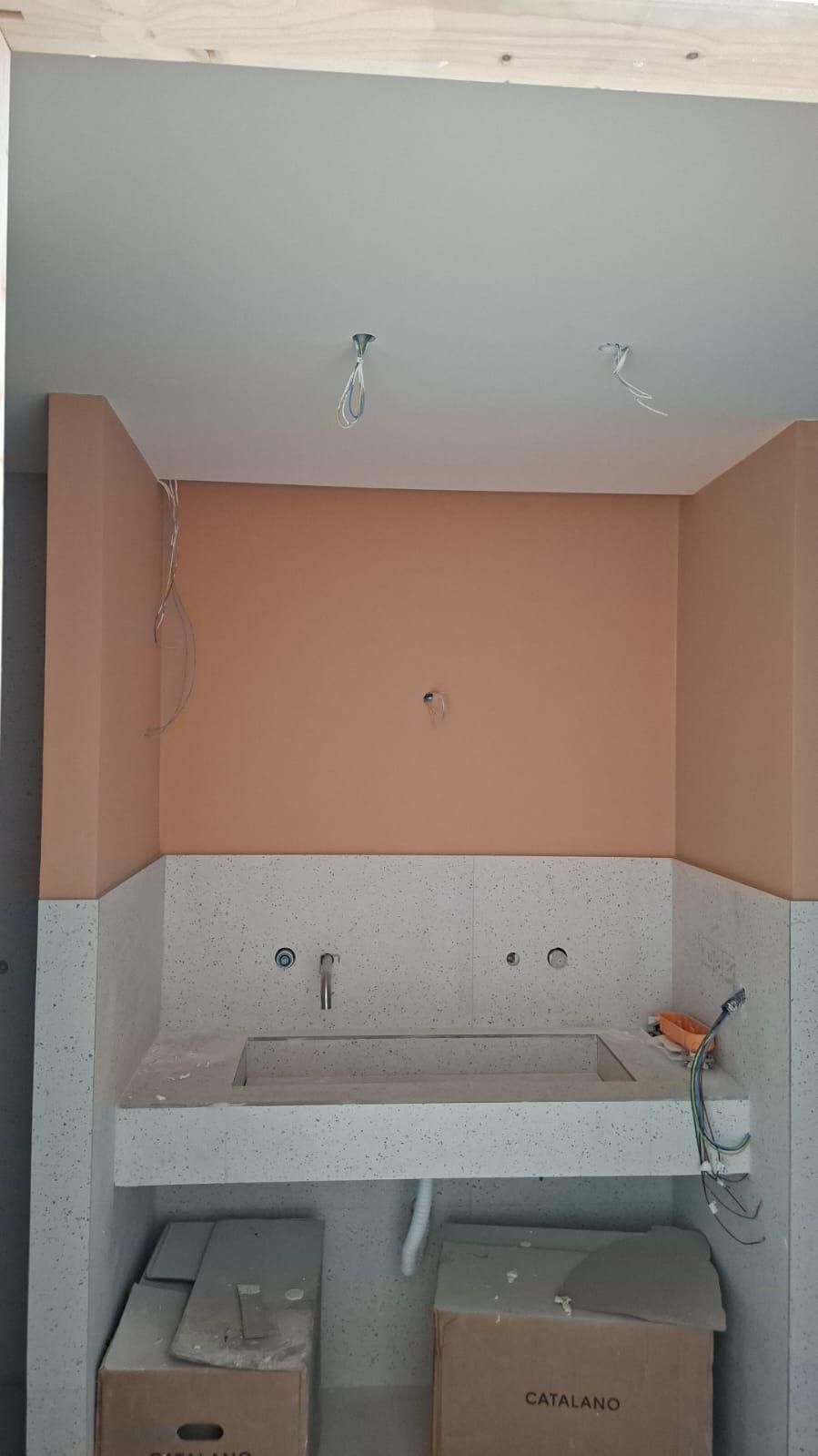 Baño en construcción; paredes de color melocotón claro sobre un lavabo de terrazo; paredes blancas debajo.