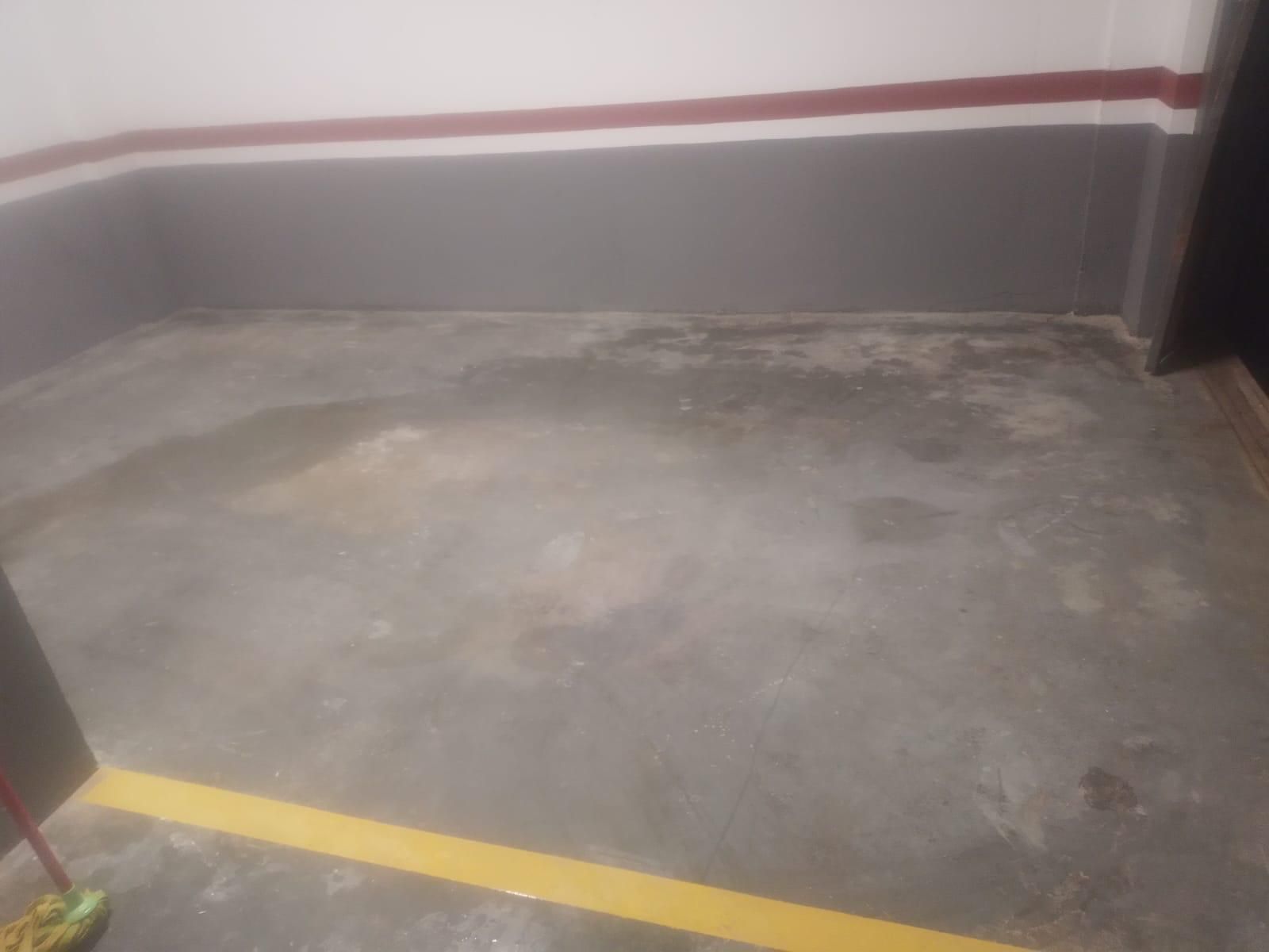 Piso de concreto en un área de estacionamiento con una franja amarilla, paredes grises y una franja roja cerca del techo.