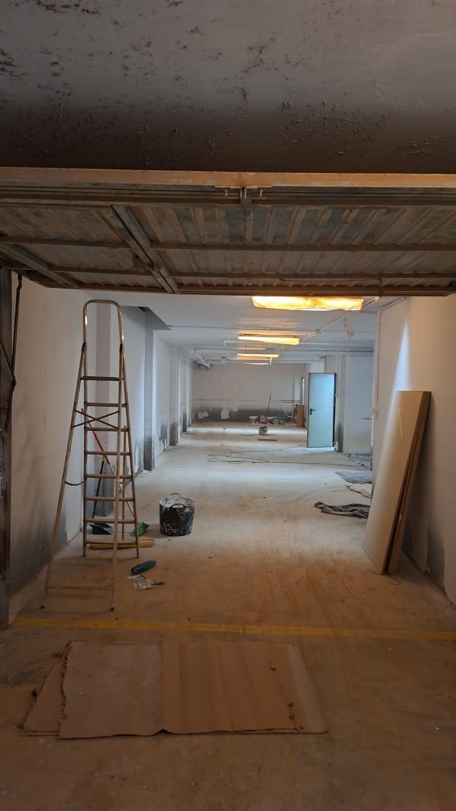 Espacio interior en proceso de renovación, con vigas de techo a la vista, escalera y materiales de construcción.