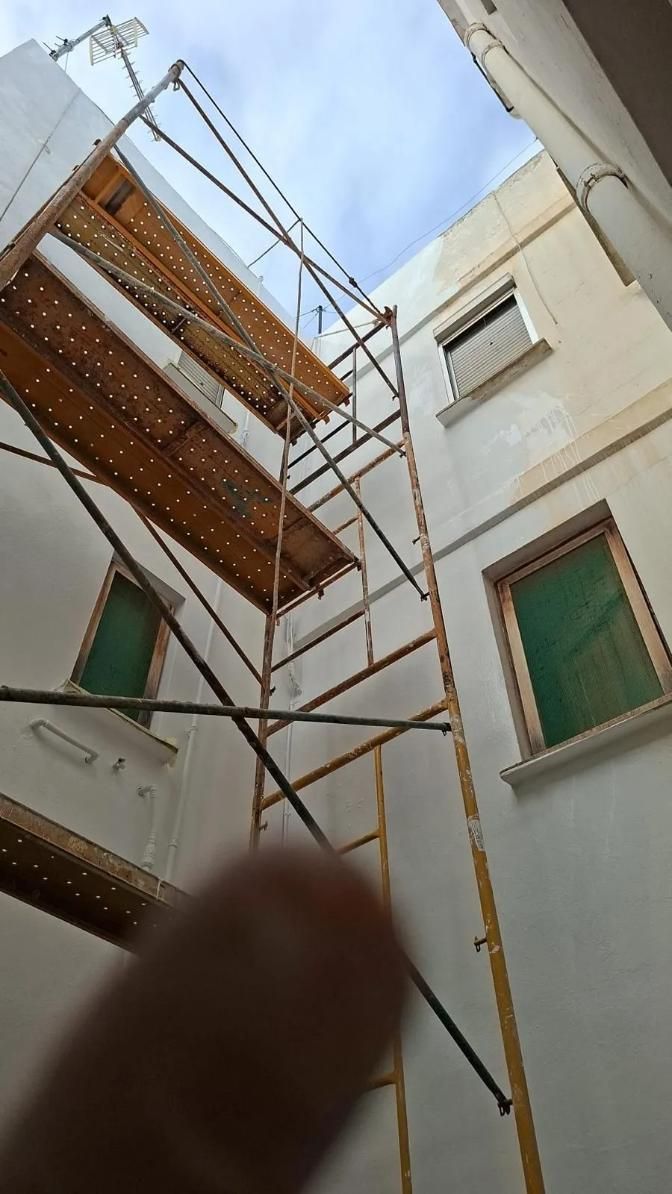 Andamio contra un edificio blanco, con el cielo visible. Dos cortinas verdes.