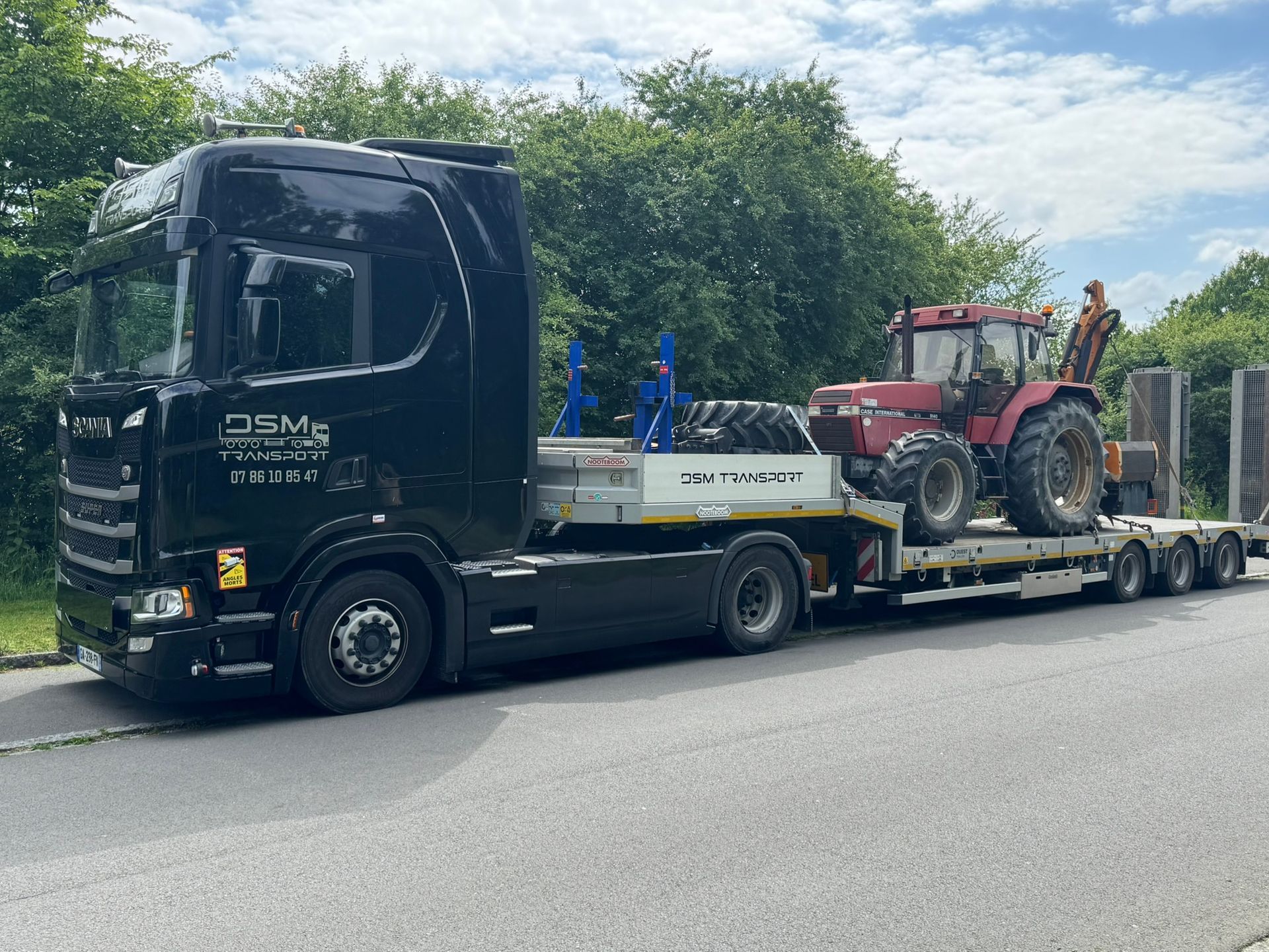 Un semi-remorque noir tirant une remorque à plateau avec un tracteur rouge.