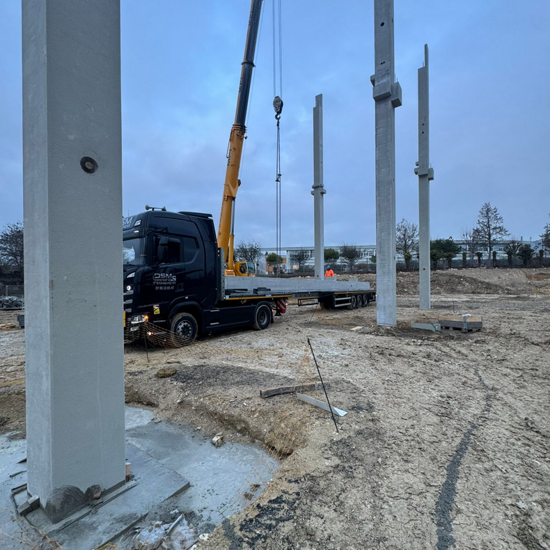 Chantier de construction avec camion-grue soulevant une poutre en béton.