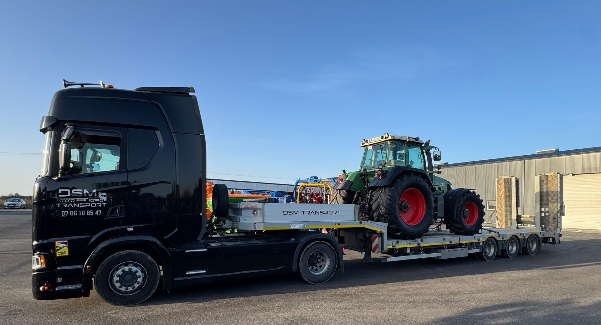 Une dépanneuse noire transporte un tracteur vert sur une remorque à plateau.