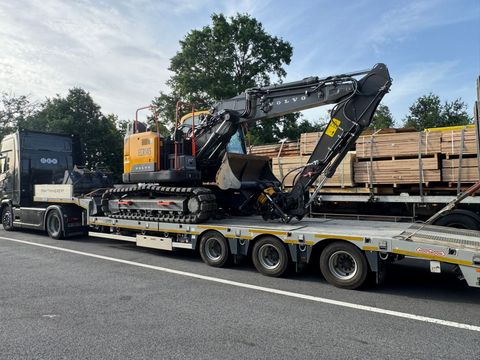 Une excavatrice noire chargée sur une remorque à plateau.