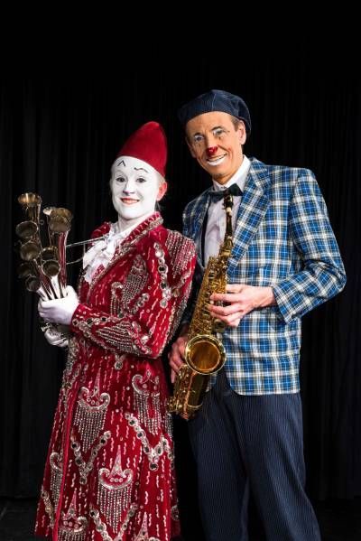 Un clown tient un saxophone à côté d'un homme portant une veste à carreaux.