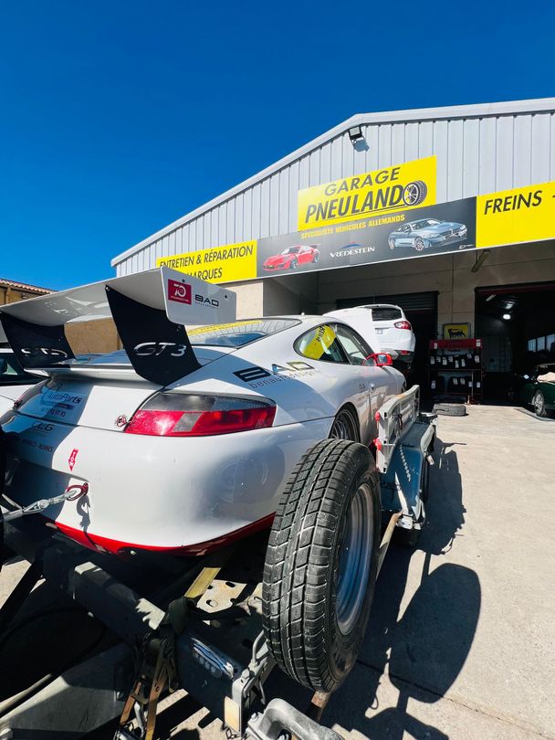 Voiture de sport rouge garée devant un garage, panneau PNEU LAND.