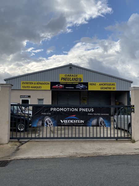 Garage Predilano avec portail noir, publicité pour une promotion de pneus. Bâtiment gris, ciel nuageux.