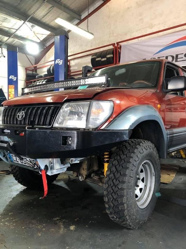 Toyota Land Cruiser orange modifié avec pare-chocs noir et gros pneus dans un garage.