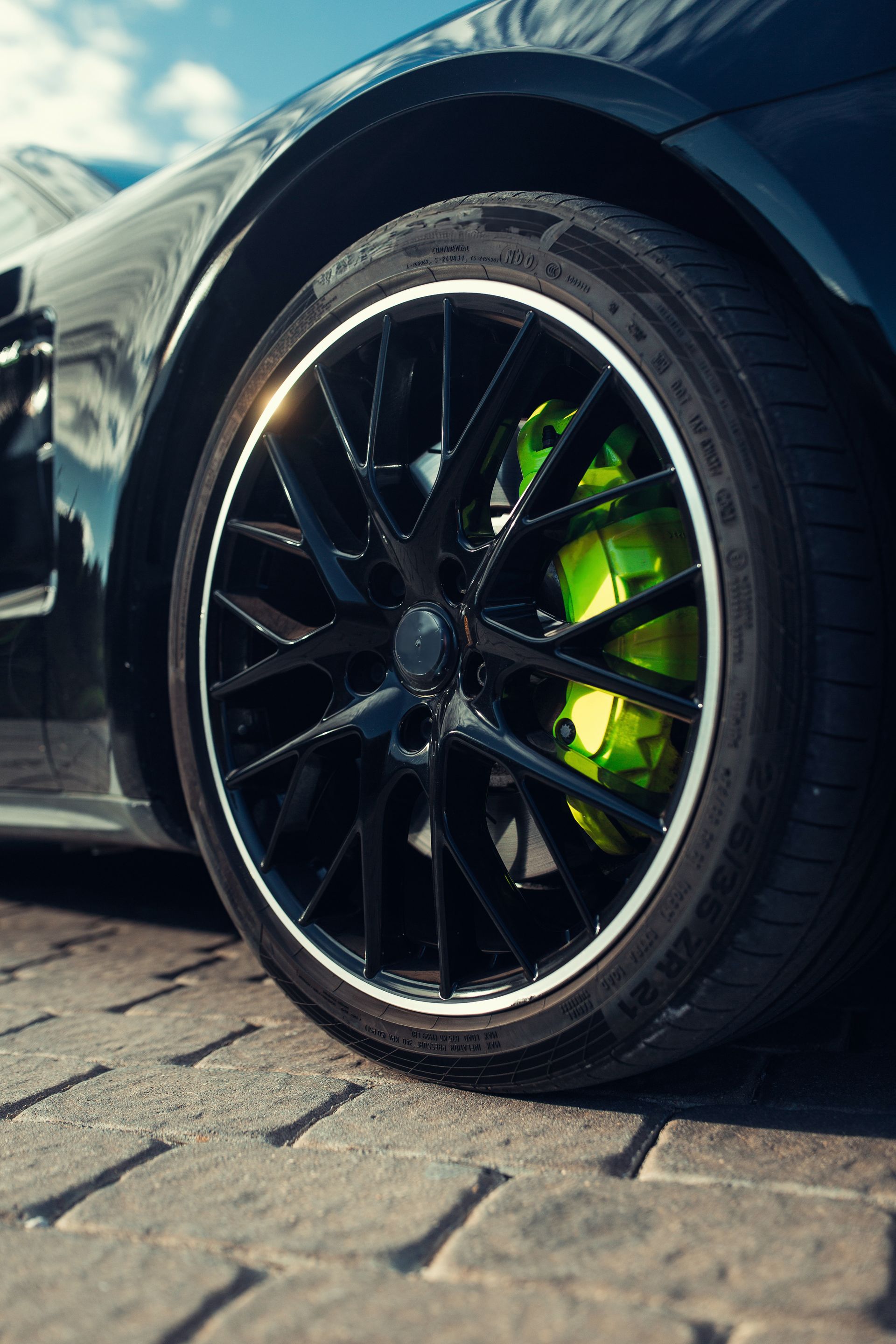 Pneu de voiture de sport noir avec étrier de frein vert fluo, sur une surface en brique.