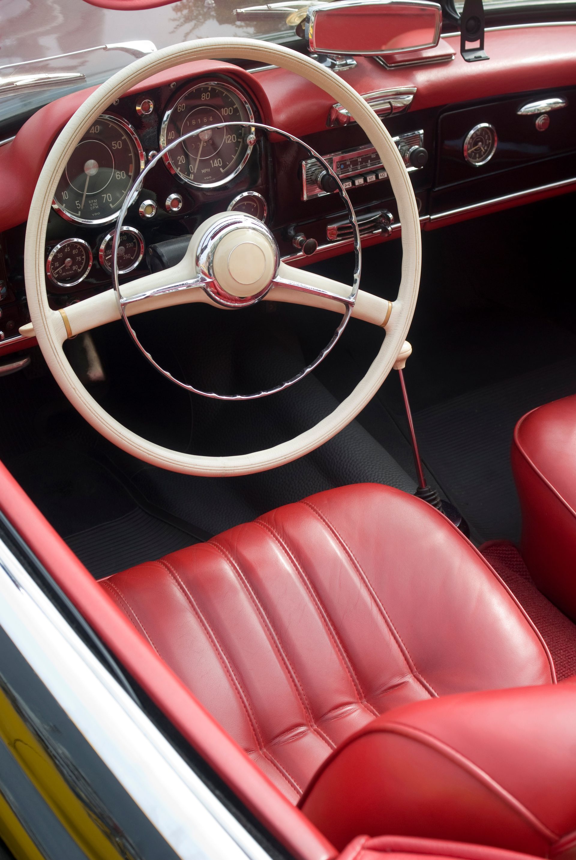 Intérieur en cuir rouge d'une voiture décapotable vintage, avec volant et tableau de bord crème.