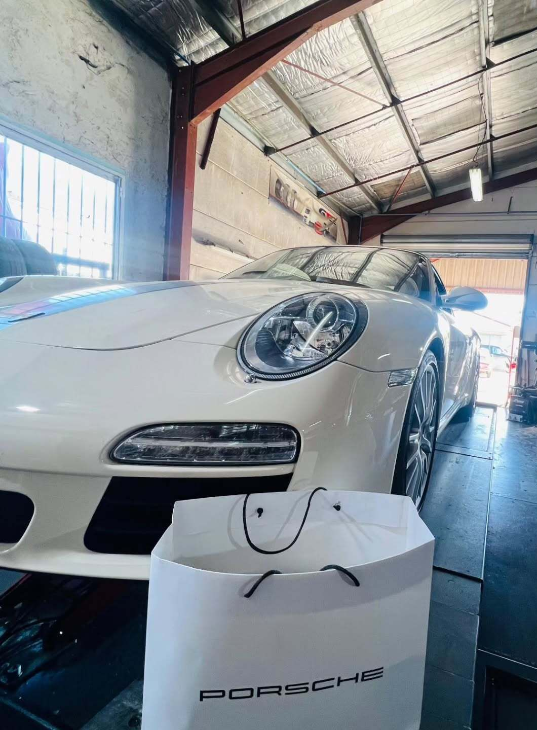 Porsche blanche garée dans un garage avec un sac cadeau Porsche au premier plan.
