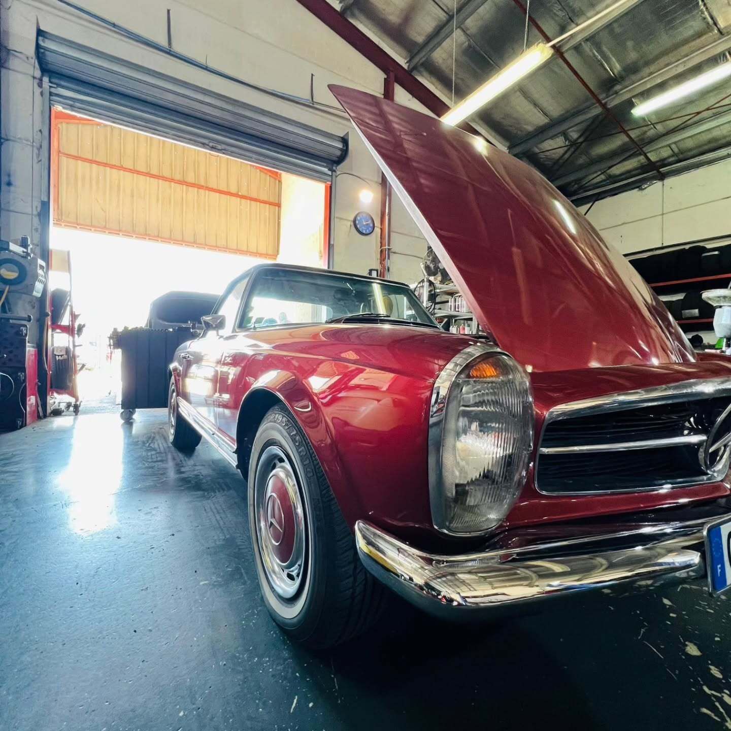 Voiture décapotable classique rouge avec capot ouvert dans un garage.
