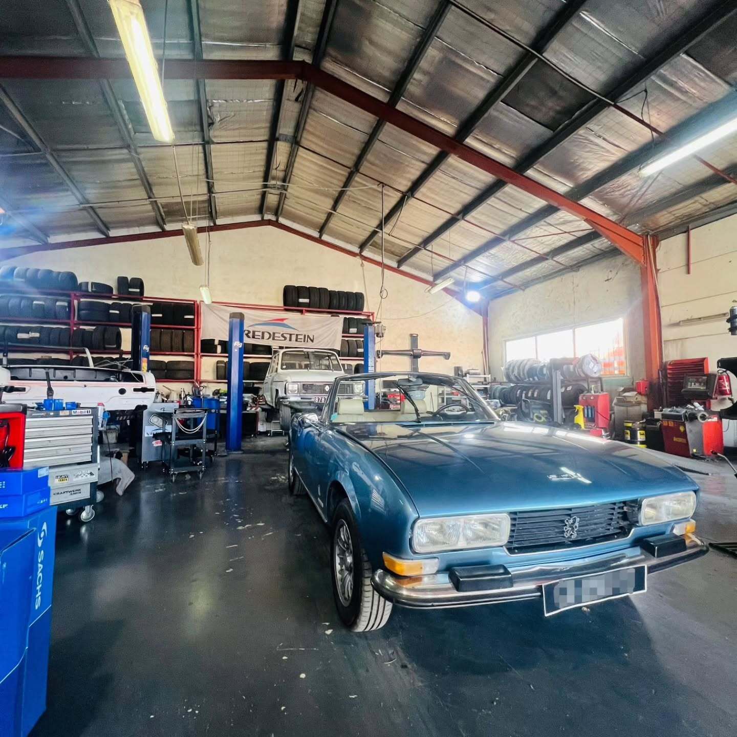 Voiture décapotable bleue à l'intérieur d'un garage, entourée d'outils et d'équipements.