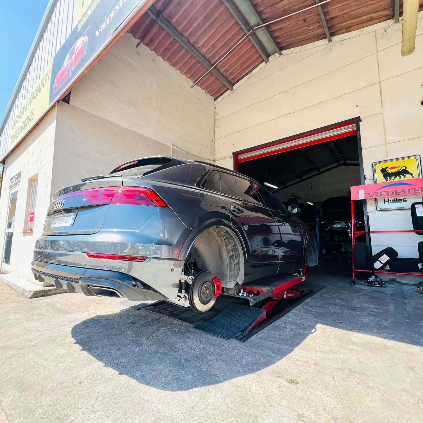Un SUV sombre sur un ascenseur à l'intérieur d'un garage, roue retirée pour entretien.