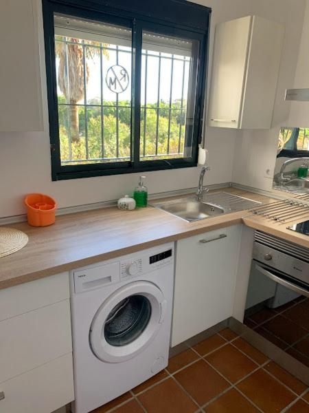 Cocina con lavadora bajo encimera, fregadero y ventana con vista al exterior.