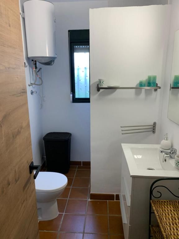 Baño con inodoro, lavabo y calentador de agua; piso de baldosas de terracota y paredes blancas.