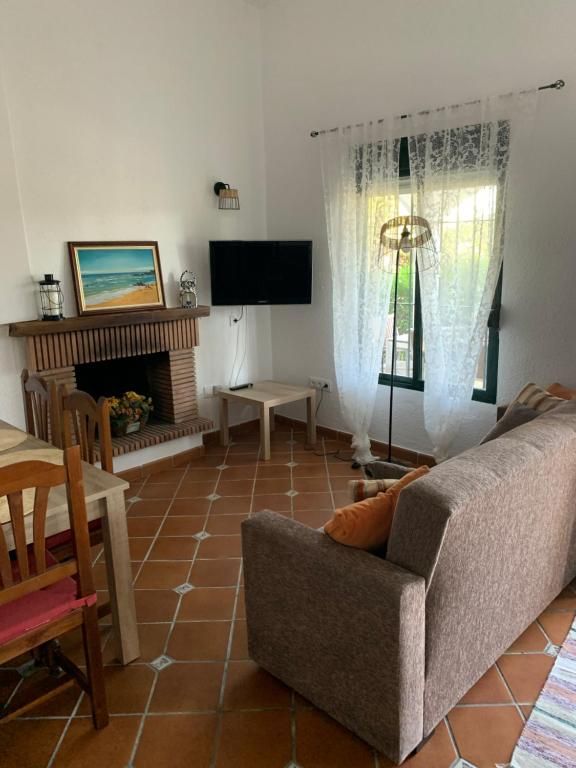 Acogedora sala de estar con chimenea, TV, sofá y mesa de comedor, con suelo de baldosas de terracota.