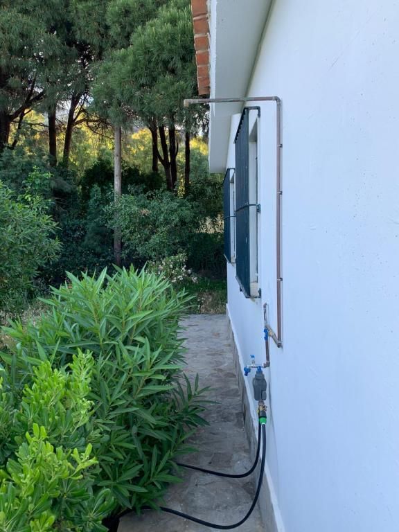 Panel solar instalado en la pared de un edificio blanco con tuberías de cobre y mangueras negras.