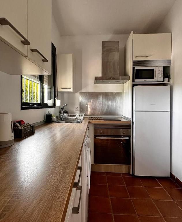 Cocina pequeña con gabinetes blancos, encimera de madera, electrodomésticos de acero inoxidable y piso de terracota.