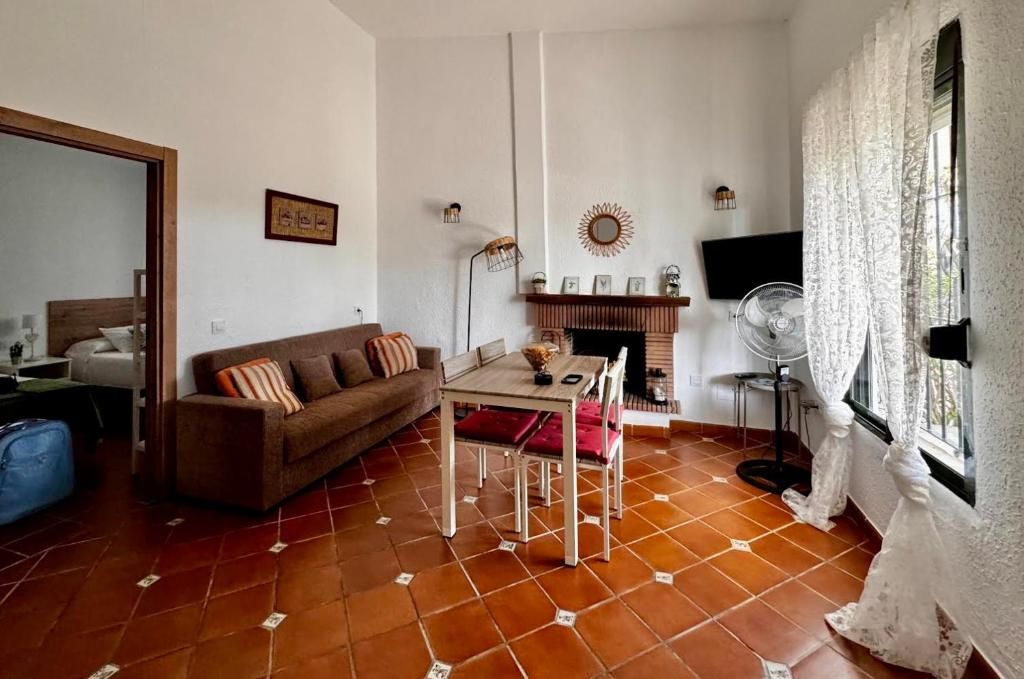 Sala de estar con piso de baldosas marrones, sofá, mesa, chimenea y ventana con cortinas de encaje.
