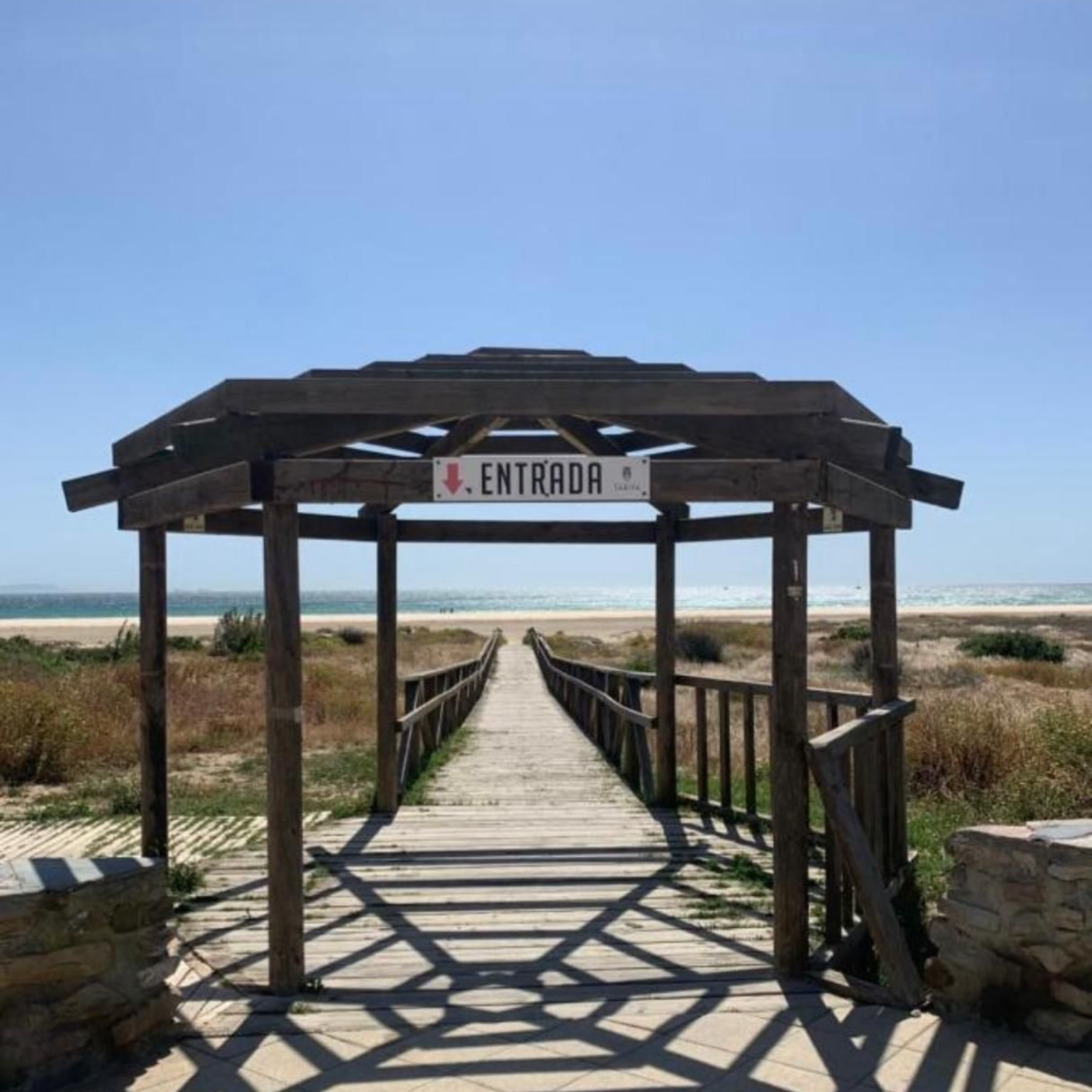 Una pasarela de madera conduce a la playa bajo un arco denominado