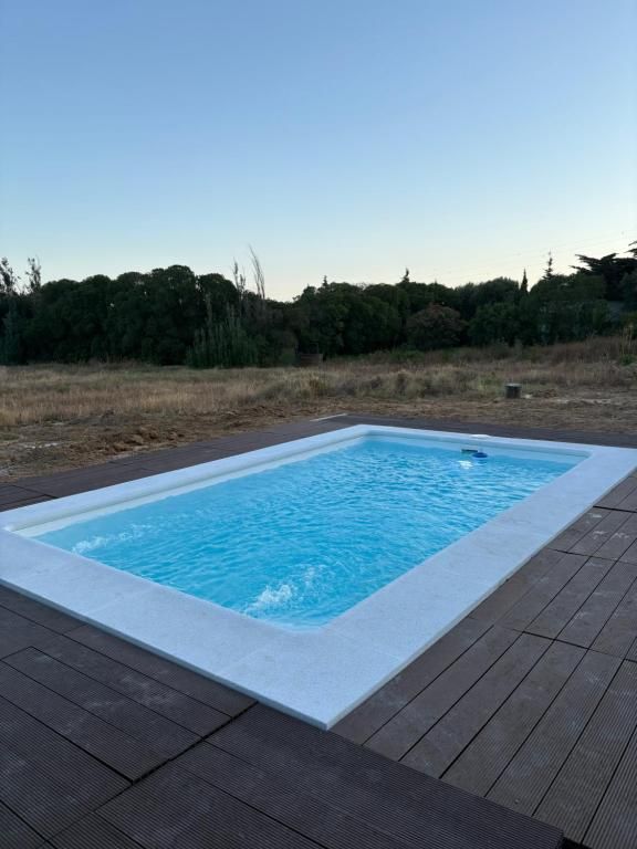 Piscina rectangular de agua azul y borde blanco rodeada de tarima de madera oscura y un campo de césped.