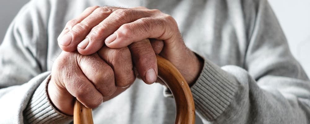 Mains d'une personne âgée posées sur sa cane en bois