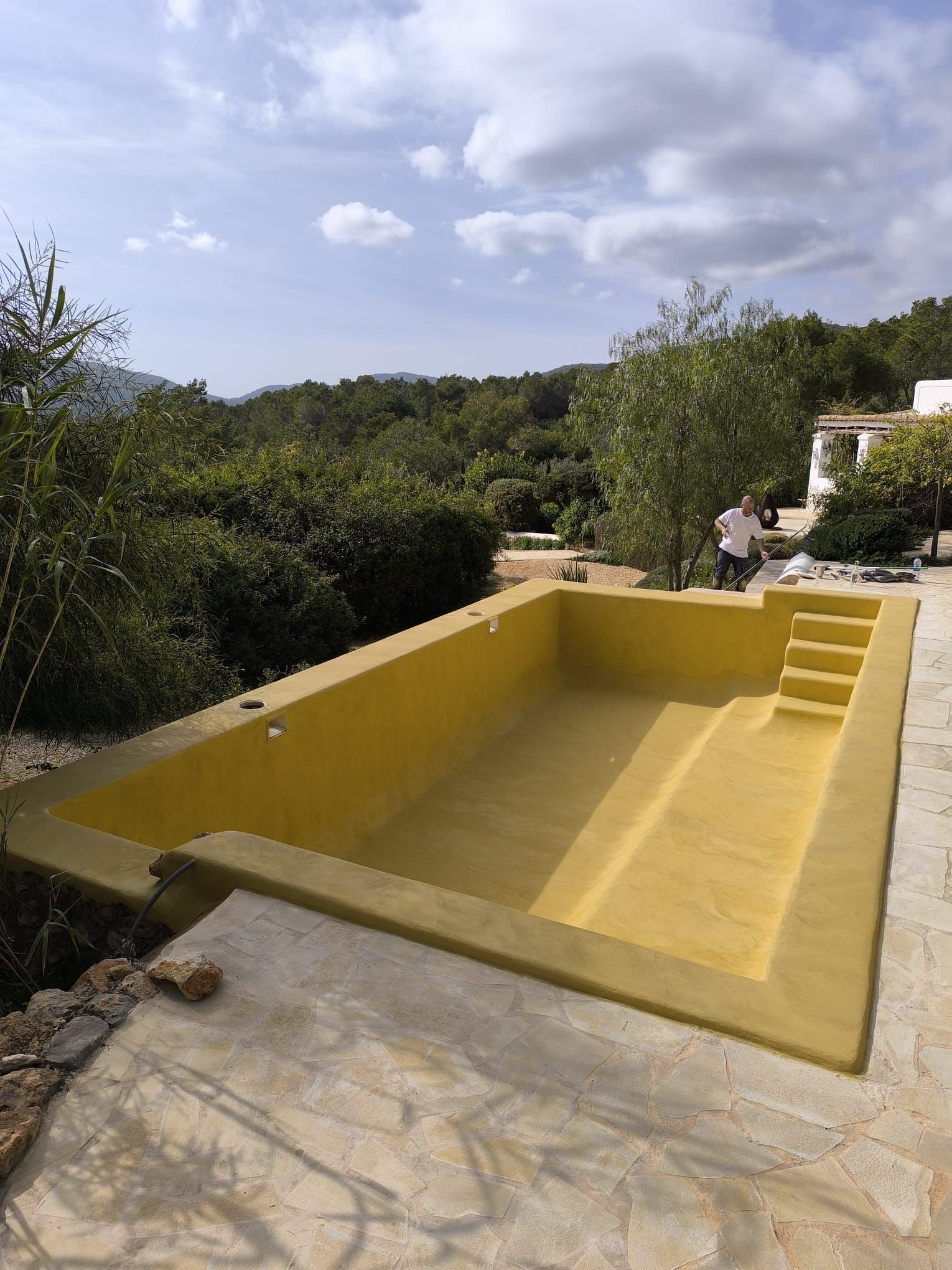 Piscina amarilla vacía en un entorno al aire libre con escaleras y un hombre al fondo.