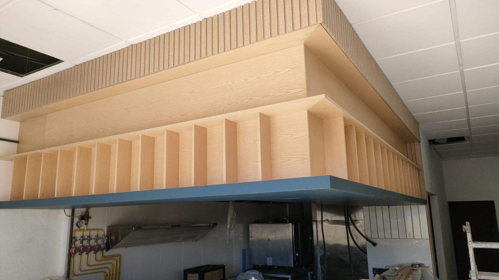 Estructura de madera empotrada en el techo, posiblemente para almacenaje o decoración, con base azul y compartimentos beige.