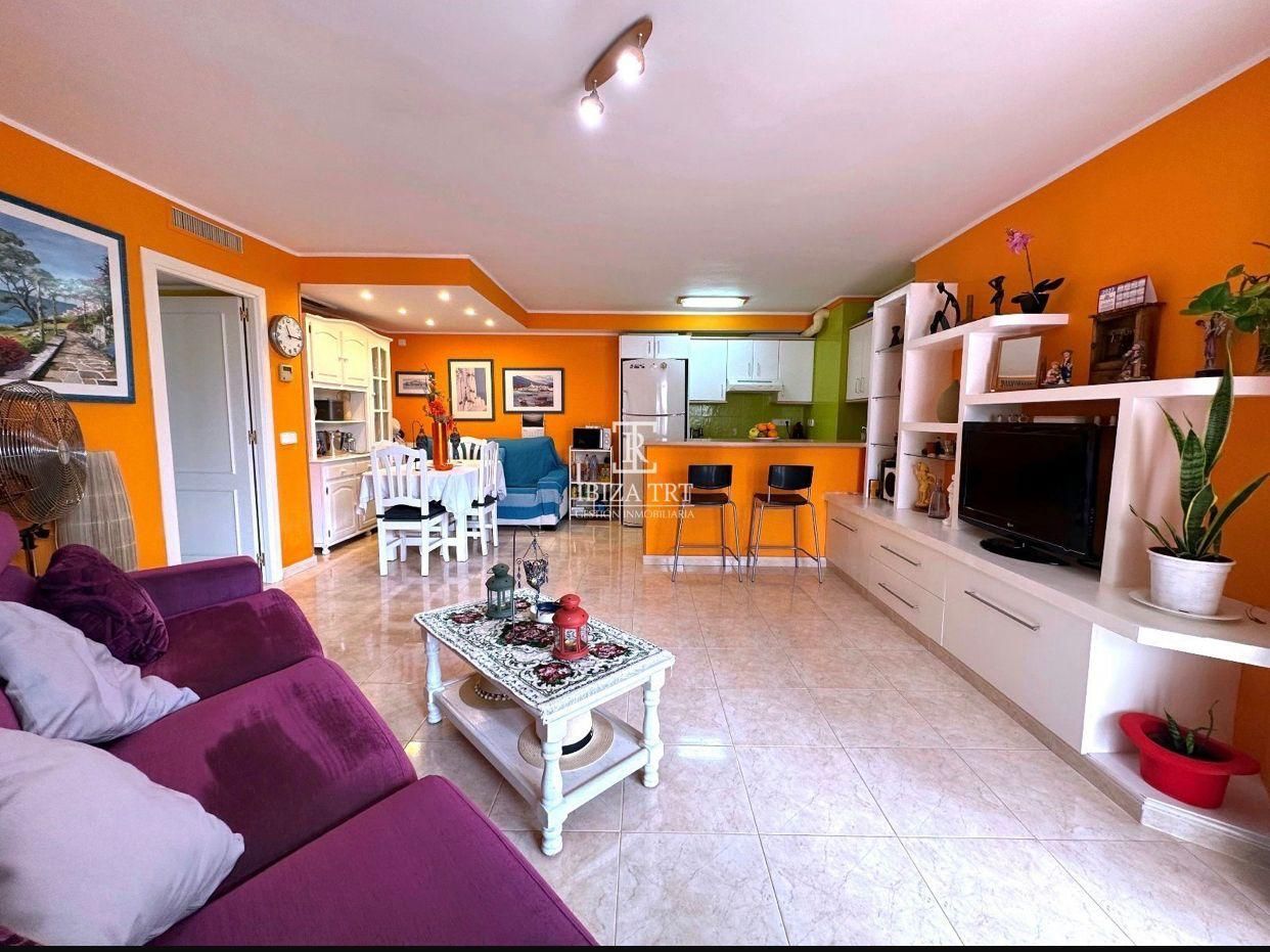 Sala de estar de color naranja brillante con sofá morado, estantes blancos y vista a la cocina y al comedor.