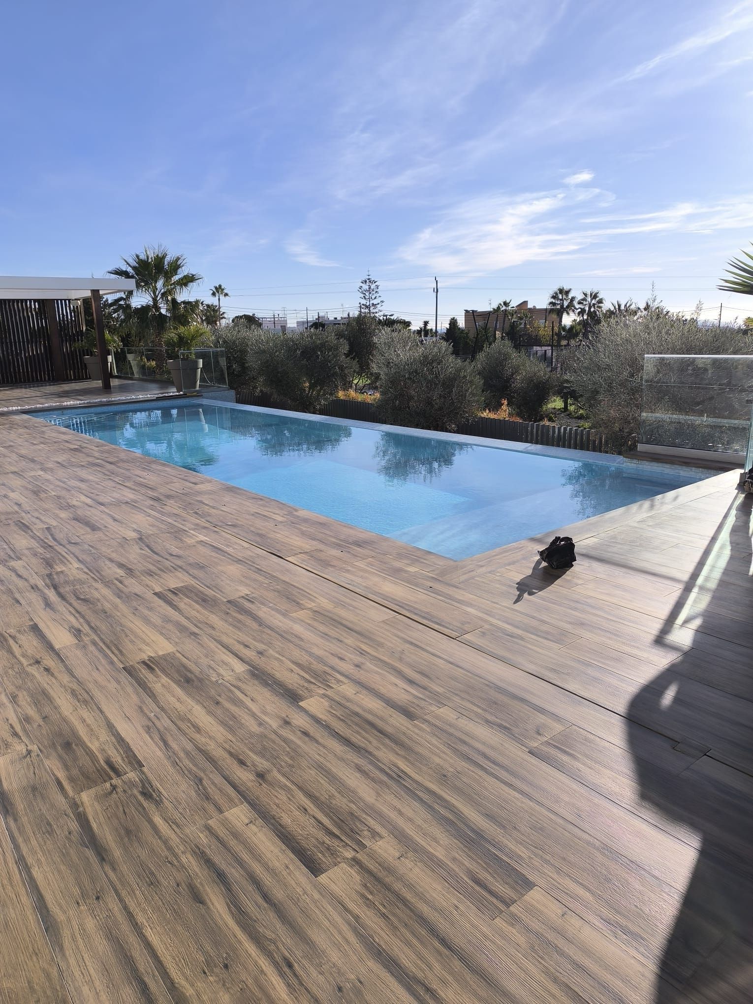 Piscina de agua azul rodeada de terraza de madera bajo un cielo azul soleado.