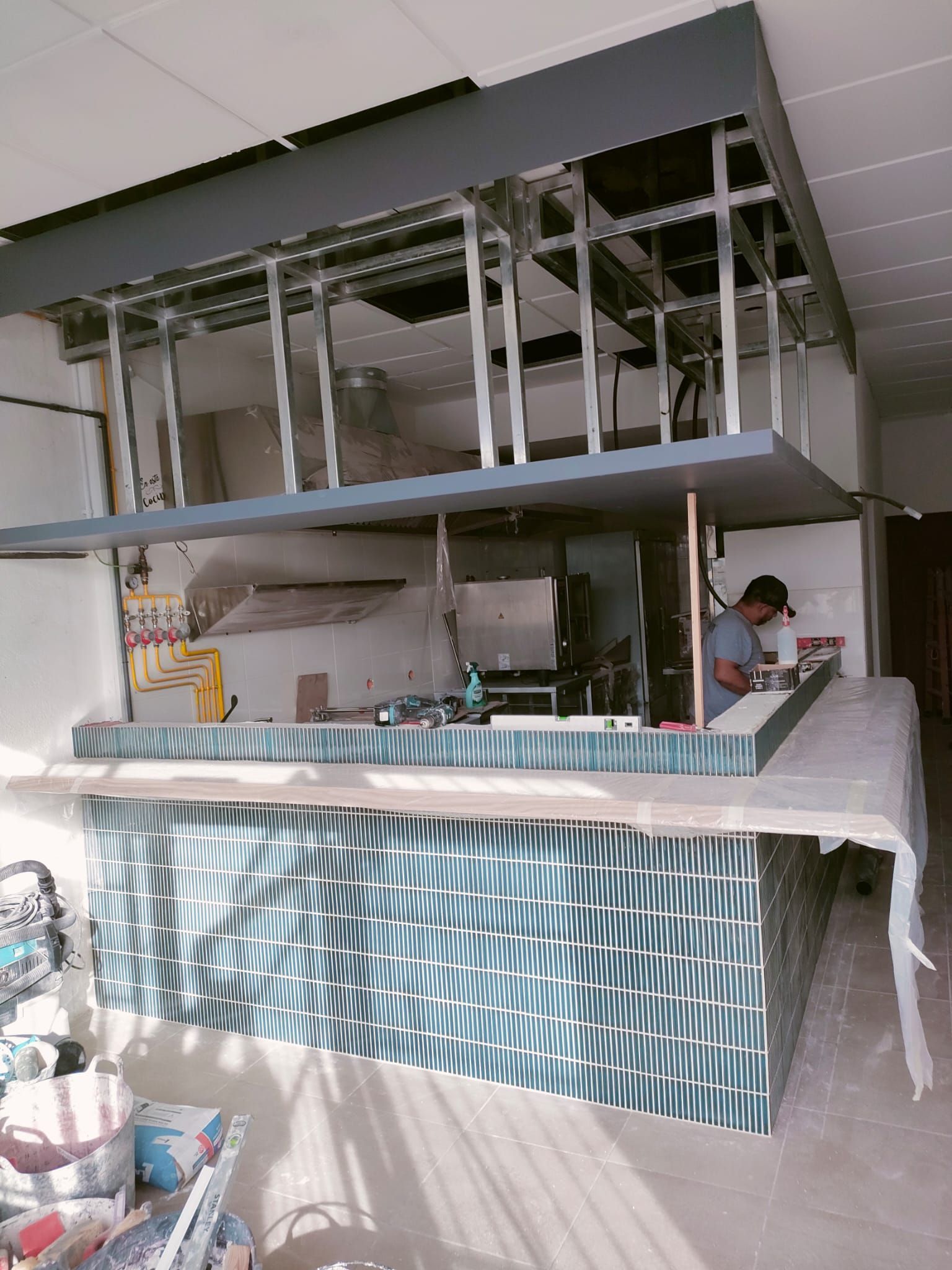 Un bar en construcción, con un frente de azulejos, una estructura elevada y un trabajador en el interior.