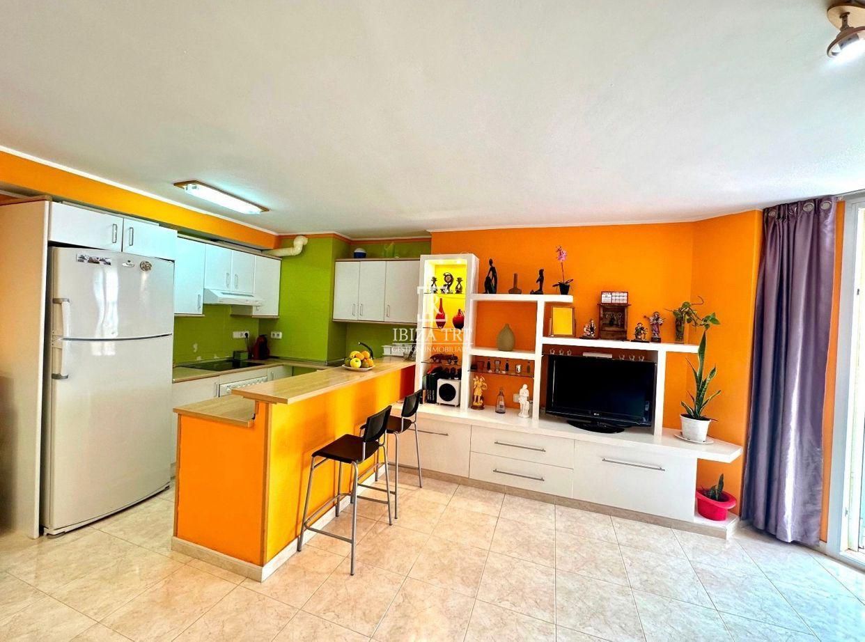 Espacio de estar abierto de colores brillantes con cocina, paredes naranjas, gabinetes blancos y una barra con taburetes.